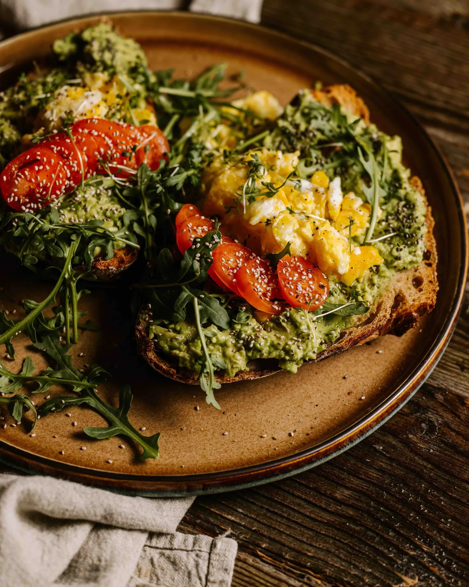 Avocado Toast mit Rührei, Paradeisern und Rucola auf einem Keramikteller