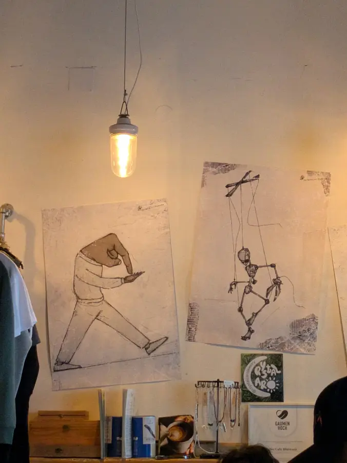 Grafische Zeichnungen an der Wand unter einer Glühbirne, darunter Schmuck und Bücher